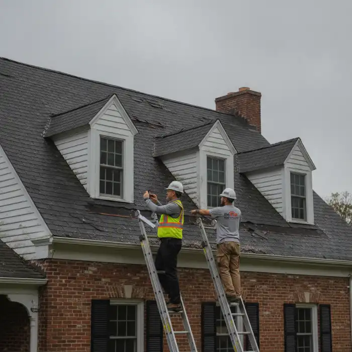 Insurance adjuster and roofing contractor on ladders inspecting wind-damaged shingles on a Connecticut colonial home
