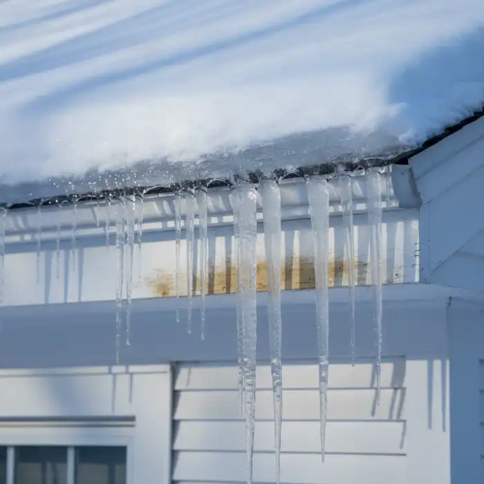 Thick ice dam and icicles along the gutter edge of a snow-covered Connecticut roof with water staining on the fascia below